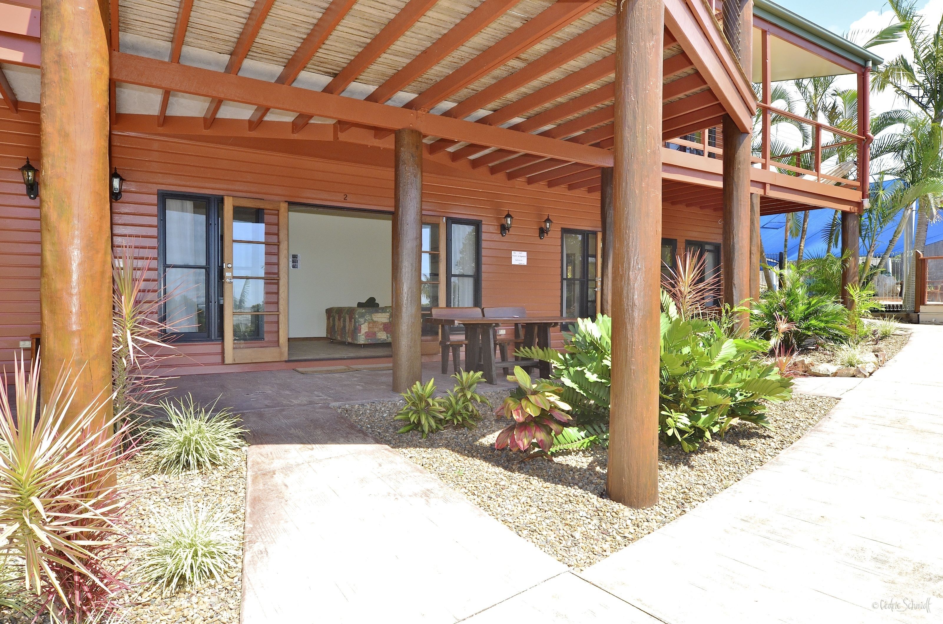 A covered outdoor area with wooden beams, a patio table, and various plants.