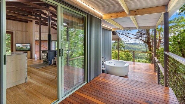 A modern outdoor living area with a wooden deck, a hot tub, and a glass-enclosed space with a fireplace. - Treetops Seaview Montville (Montville)