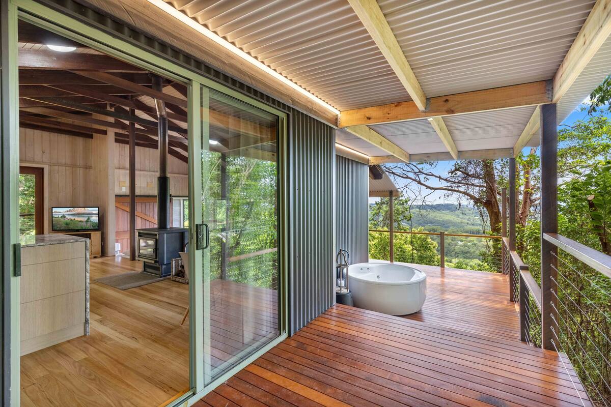 Un espace de vie extérieur moderne doté d’une terrasse en bois, d’un jacuzzi et d’un espace clos par des parois de verre, avec une cheminée.