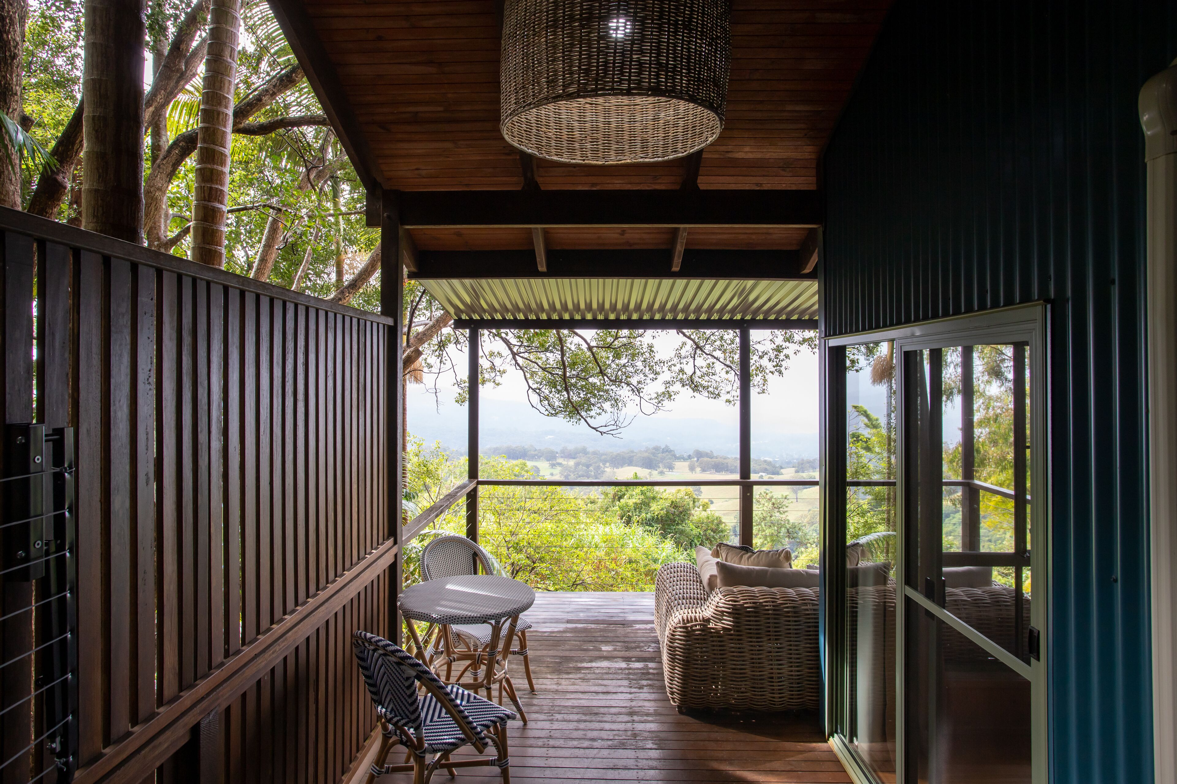 A covered outdoor area with a wooden deck, wicker furniture, and a view of the landscape.