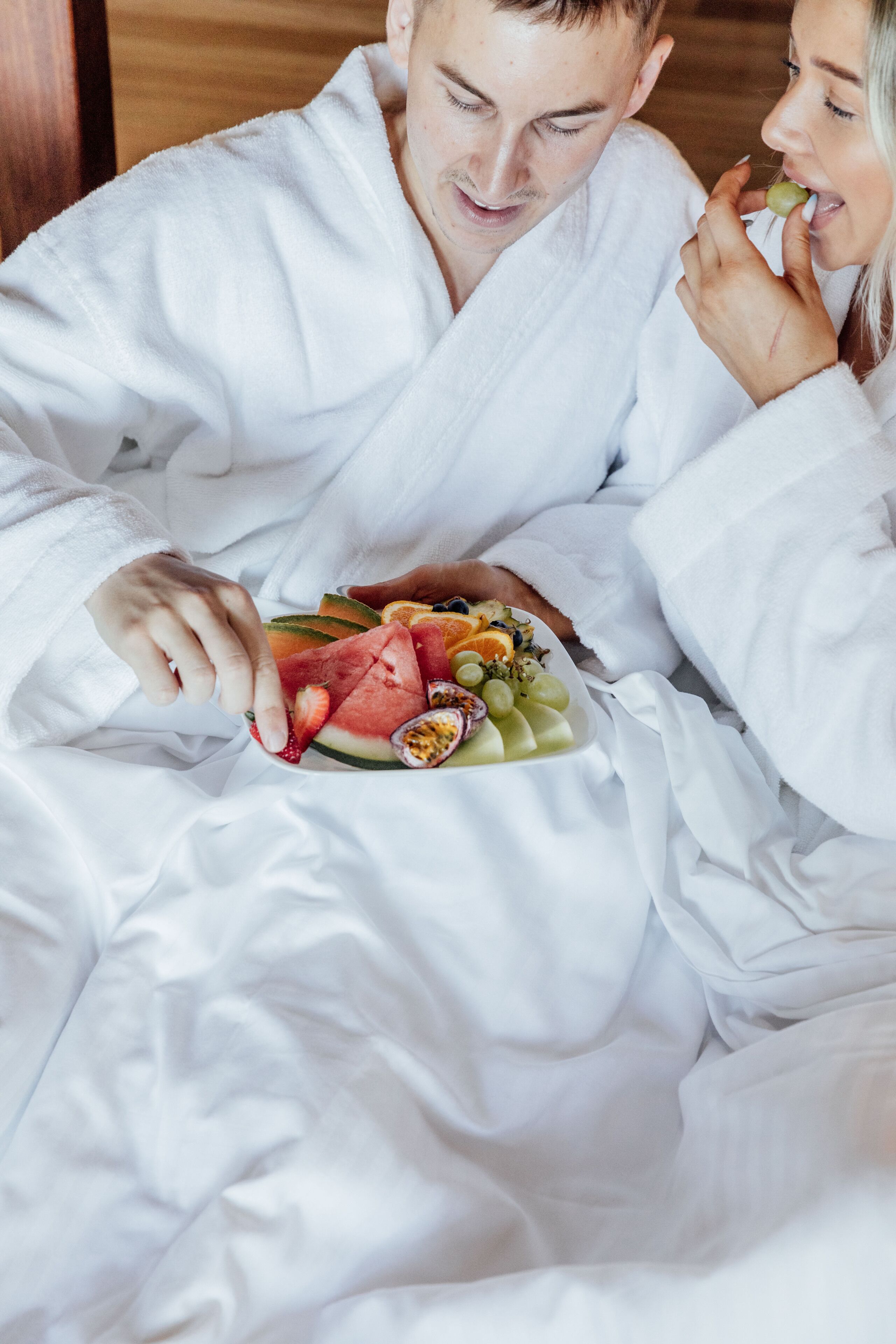 A person in a white bathrobe holding a plate of fruit.