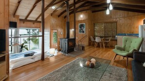 A spacious living room with wooden floors, a fireplace, a sofa, a green armchair, and a dining area with a table and chairs. - Treetops Seaview Montville (Montville)