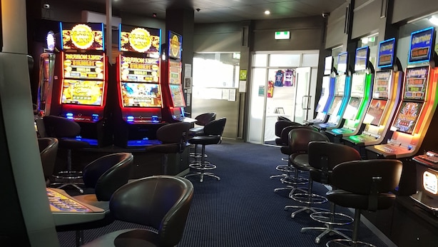 A row of slot machines in a casino with chairs and tables in the foreground. - Oonoonba Hotel Motel (Oonoonba)