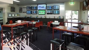 A restaurant with multiple tables and chairs, a counter, and several screens displaying content on the wall. - Oonoonba Hotel Motel (Oonoonba)