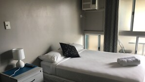 A hotel room with a bed, a bedside table with a lamp, a dresser, and a window with curtains. - Oonoonba Hotel Motel (Oonoonba)