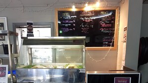 A food service area with a menu board, a grill display, and promotional posters for lunch and dinner deals. - Oonoonba Hotel Motel (Oonoonba)
