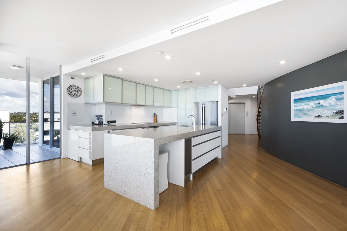 A modern kitchen with a large island, white cabinetry, and a view to the outdoors.