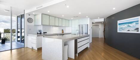 A modern kitchen with a large island, white cabinetry, and a view to the outdoors.