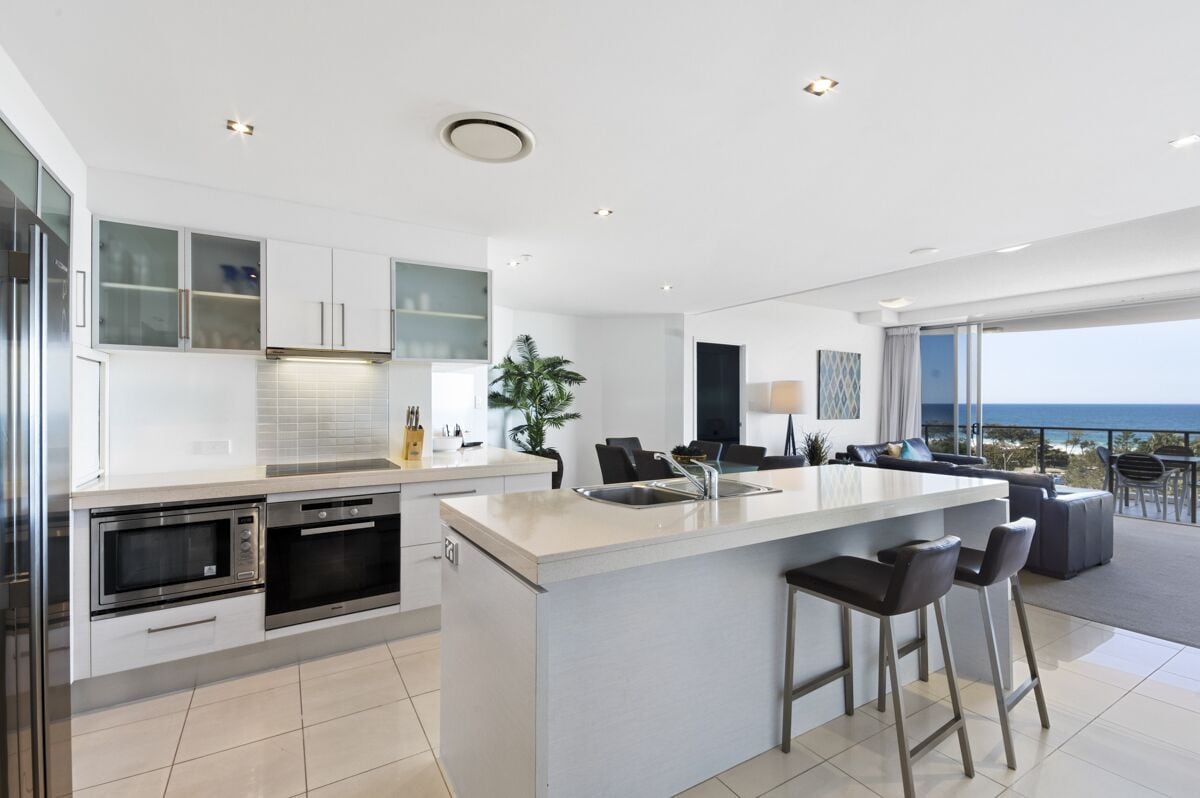 Una cocina moderna con una isla central, electrodomésticos integrados y un amplio ventanal con vistas al mar.