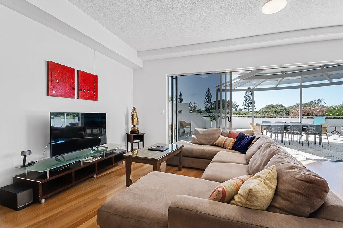 Una sala de estar moderna con un televisor de pantalla plana grande, un sofá seccional y una mesa de centro de vidrio.