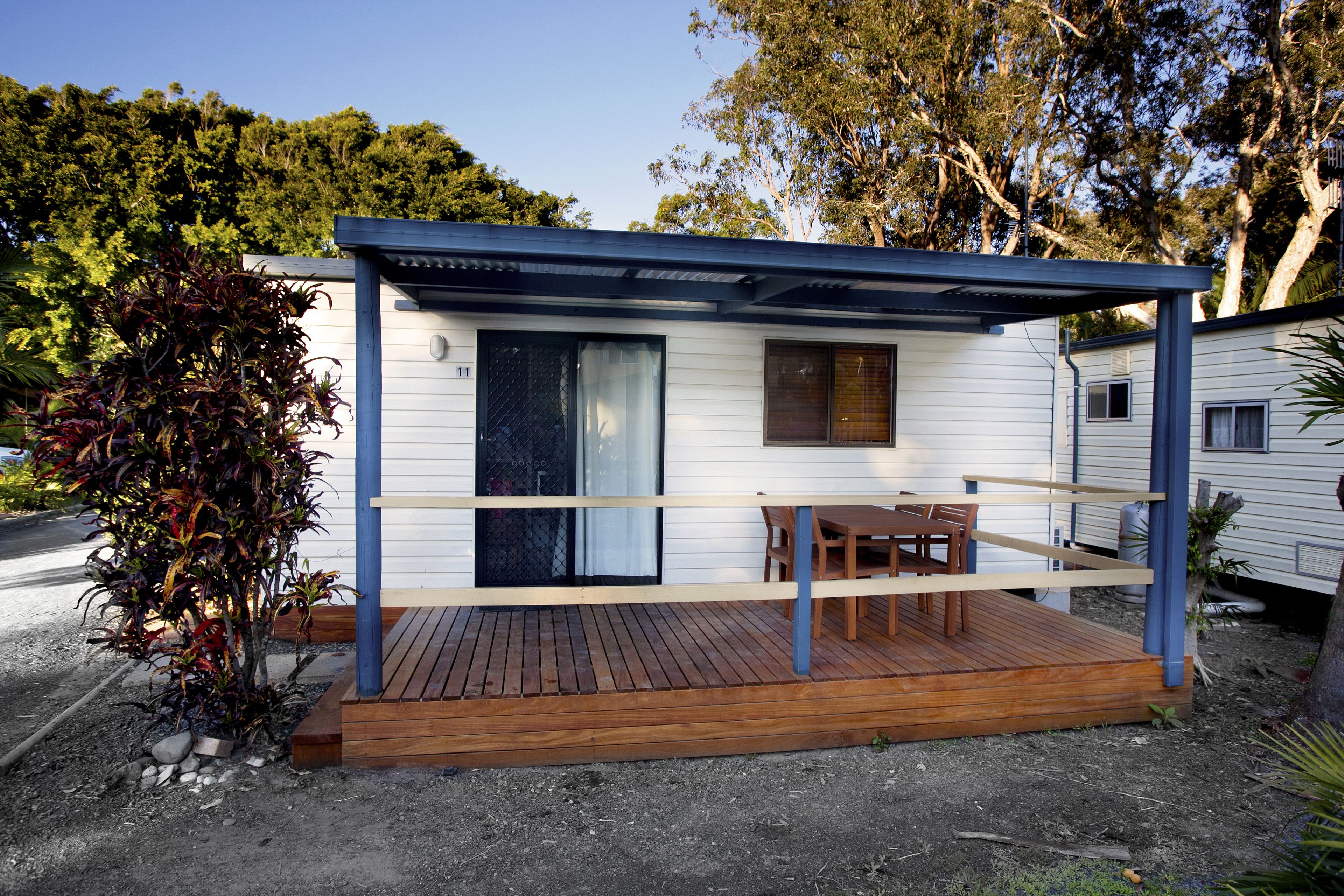 A small, single-story cabin with a wooden deck and a covered outdoor seating area.