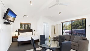 Una habitación de hotel moderna con una cama, un televisor, una mesa de comedor con sillas, un sofá y ventanas grandes.