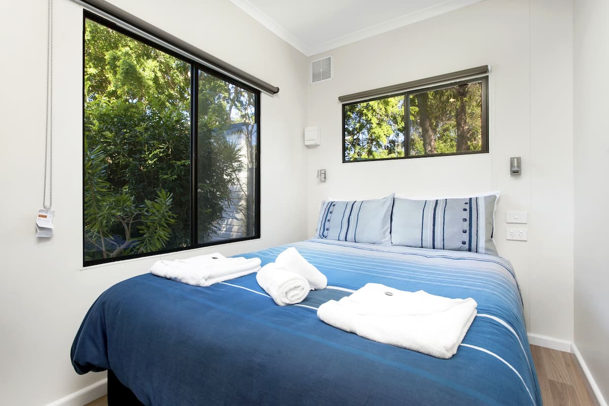 A bedroom with a large window, a bed with blue bedding, and a view of greenery outside.