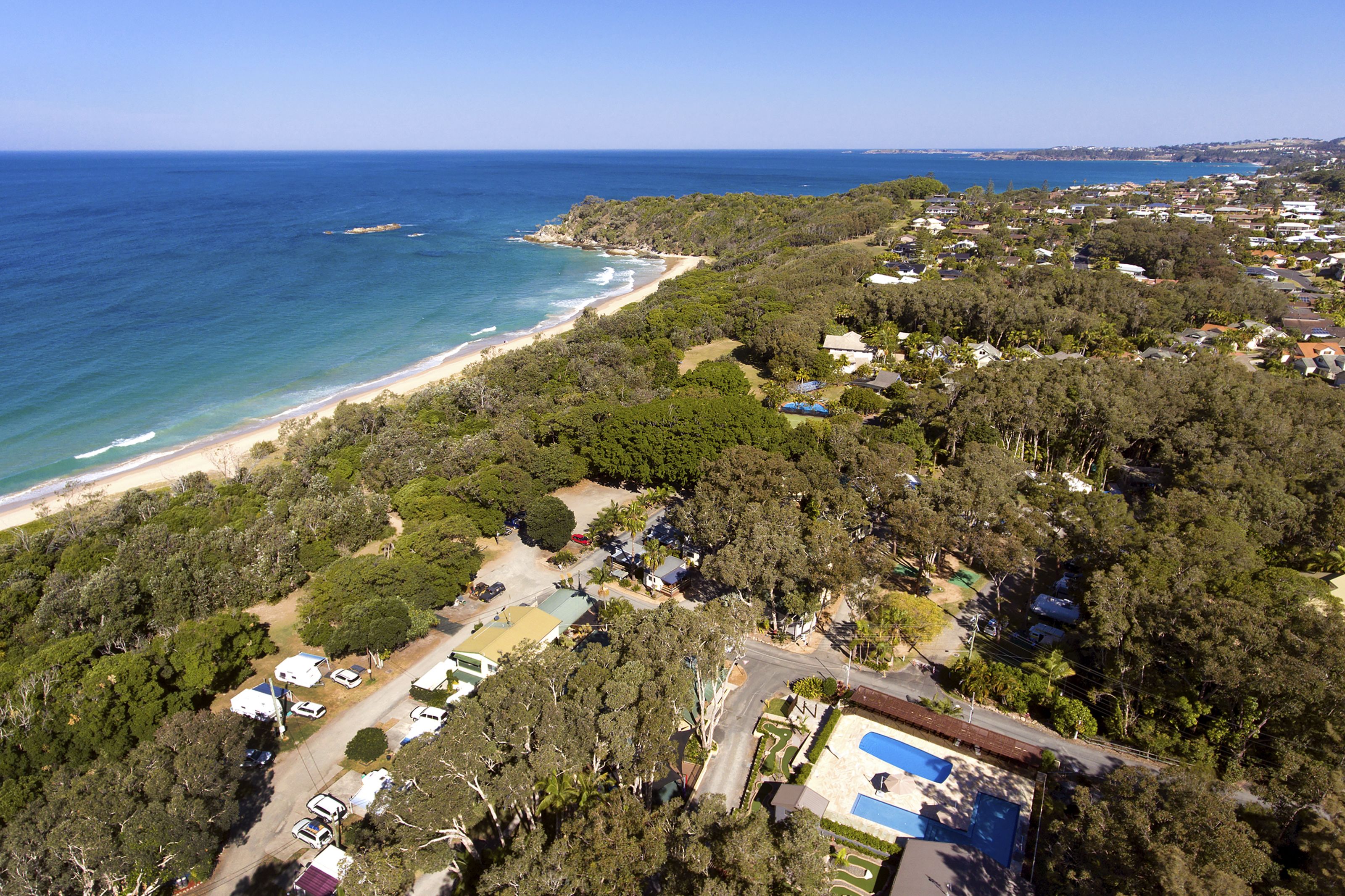 An aerial view of a coastal residential area with houses, a beach, and a swimming pool.