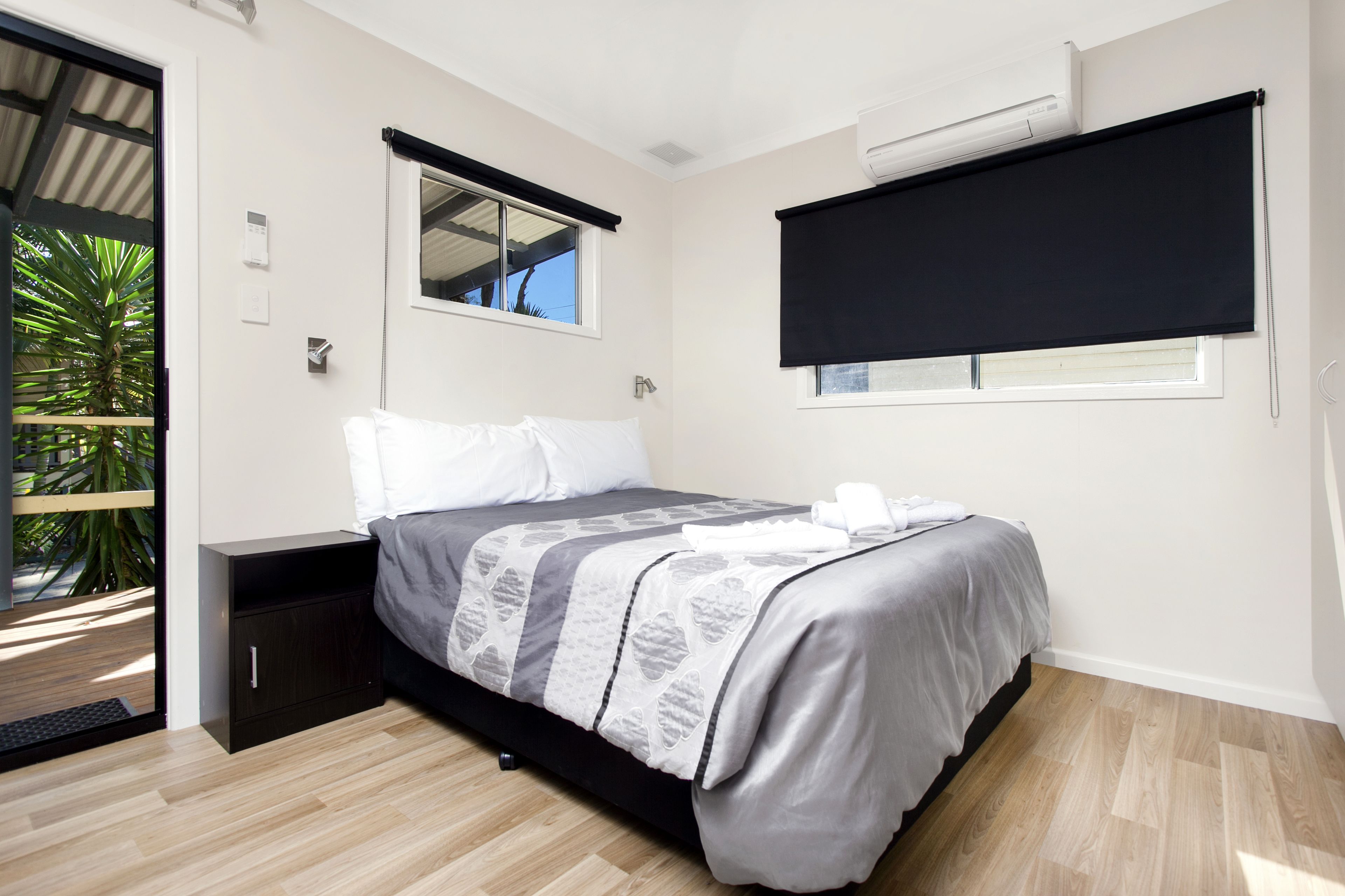 A bedroom with a bed, a nightstand, a window with a black blind, a ceiling fan, and a small potted plant.