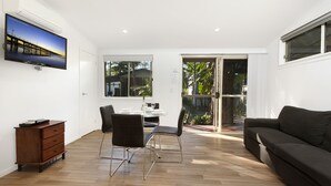 Una sala de estar moderna con un televisor de pantalla plana, un comedor con una mesa y sillas, un sofá oscuro y suelo de madera.