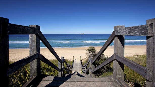 Una escalera de madera que conduce a una playa con vista despejada al océano.