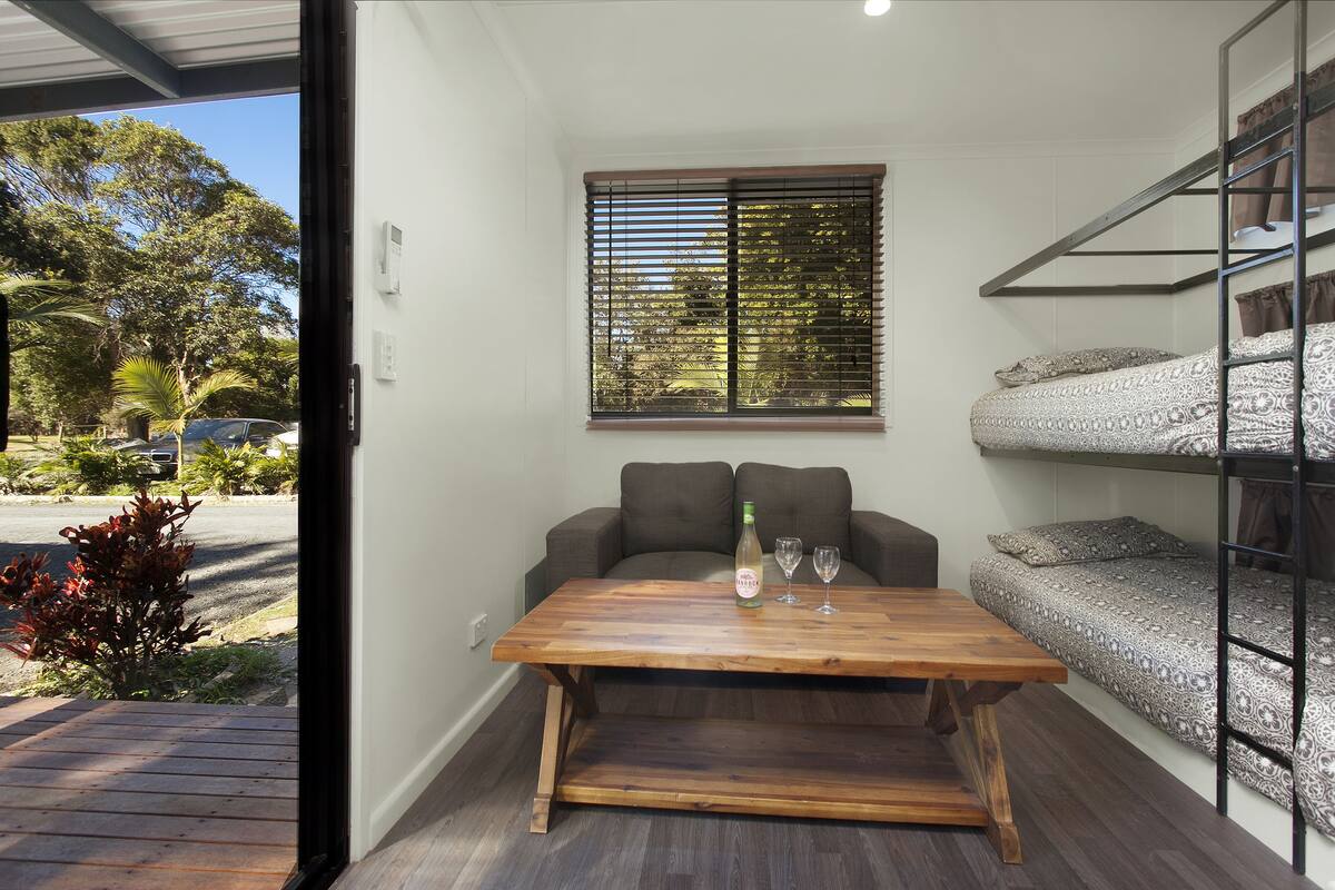A compact room with a wooden table, a sofa, and a bunk bed with patterned bedding.