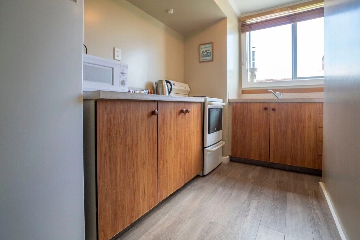 A kitchen with wooden cabinets, a microwave, a stove, and a window with blinds.