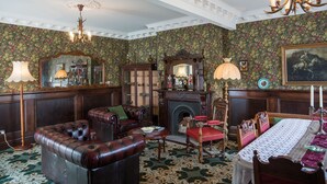 A traditional room with a fireplace, leather furniture, and ornate wallpaper.