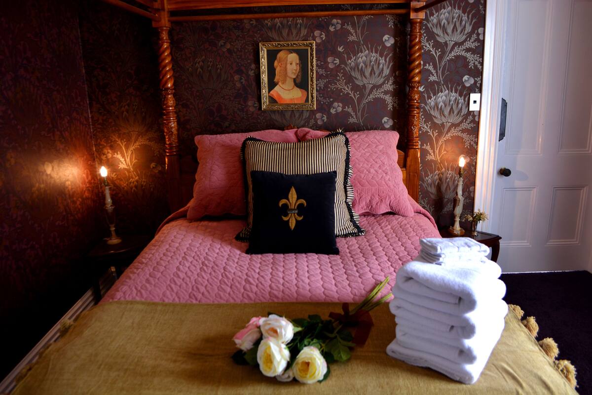 Un dormitorio con una cama con dosel, un retrato en la pared y un ramo de flores sobre la cama.