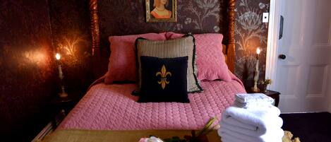 A bedroom with a four-poster bed, a portrait on the wall, and a bouquet of flowers on the bed.