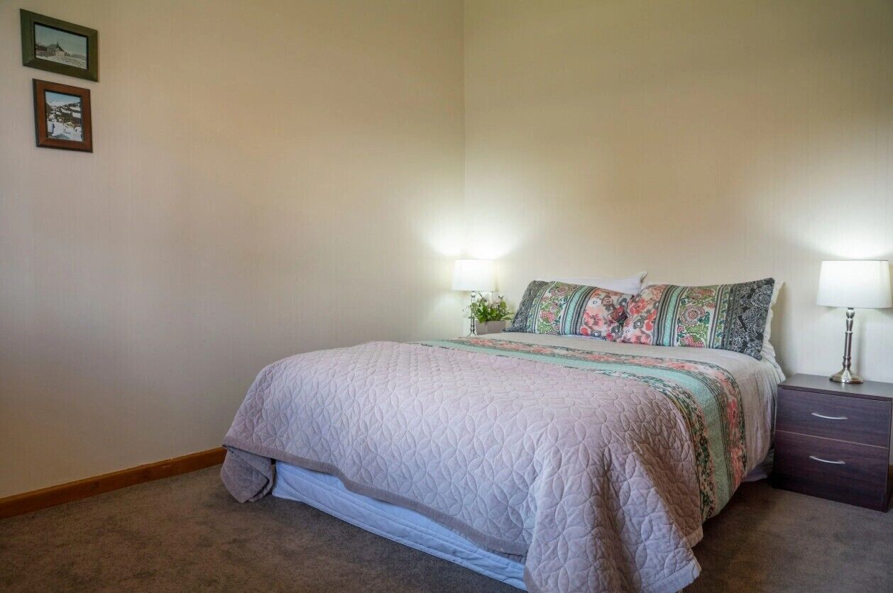 A bedroom with a bed, two bedside tables, and two wall-mounted lamps.