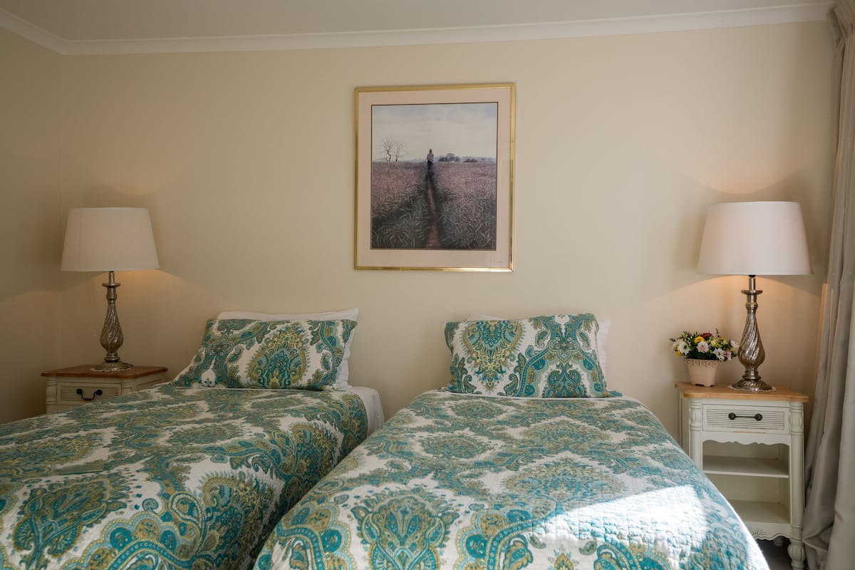 Habitación de hotel con dos camas, cada una con cubrecama estampado, un cuadro en la pared y dos mesitas de noche con lámparas.