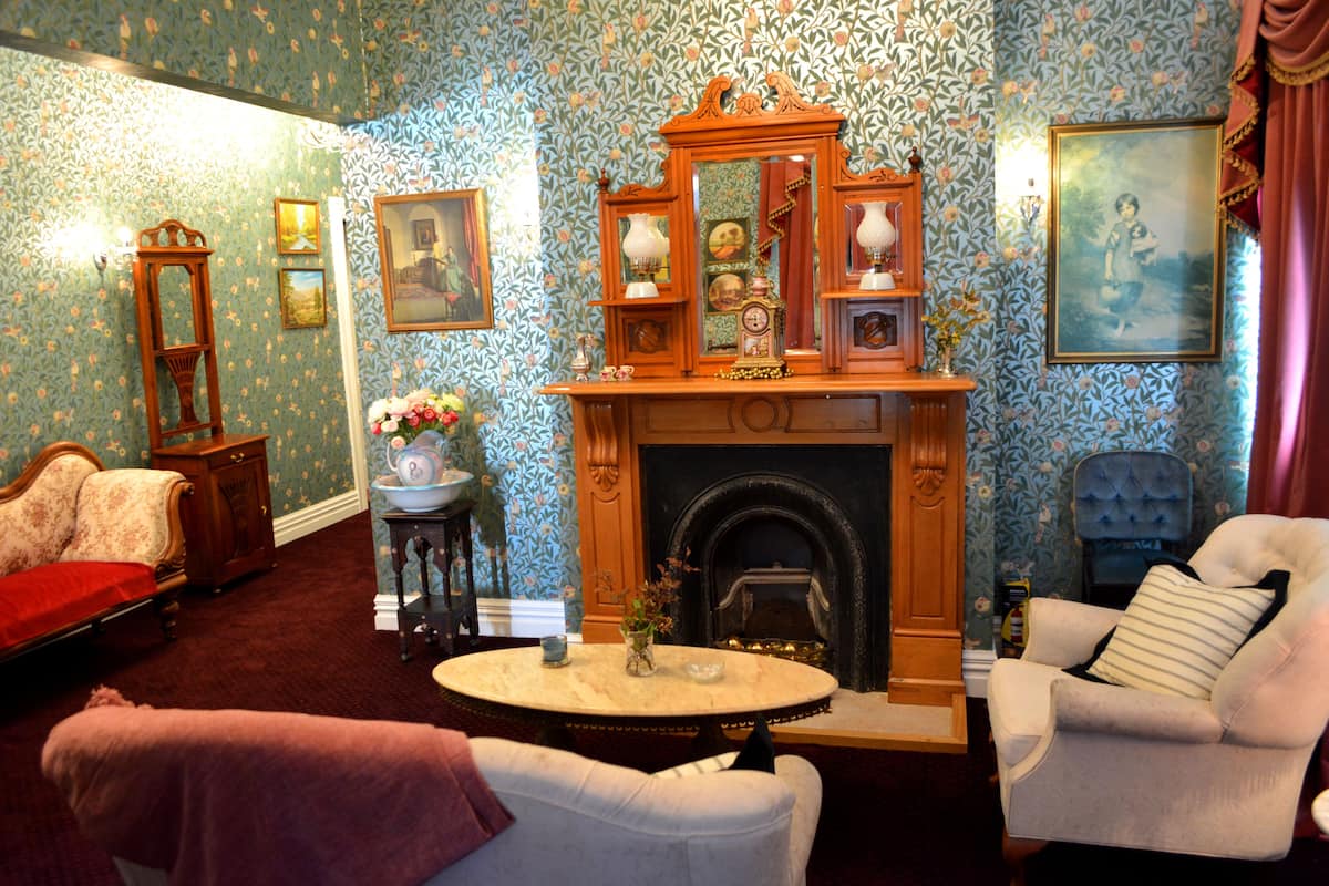 Un salón tradicional con chimenea, papel tapiz floral y muebles clásicos.