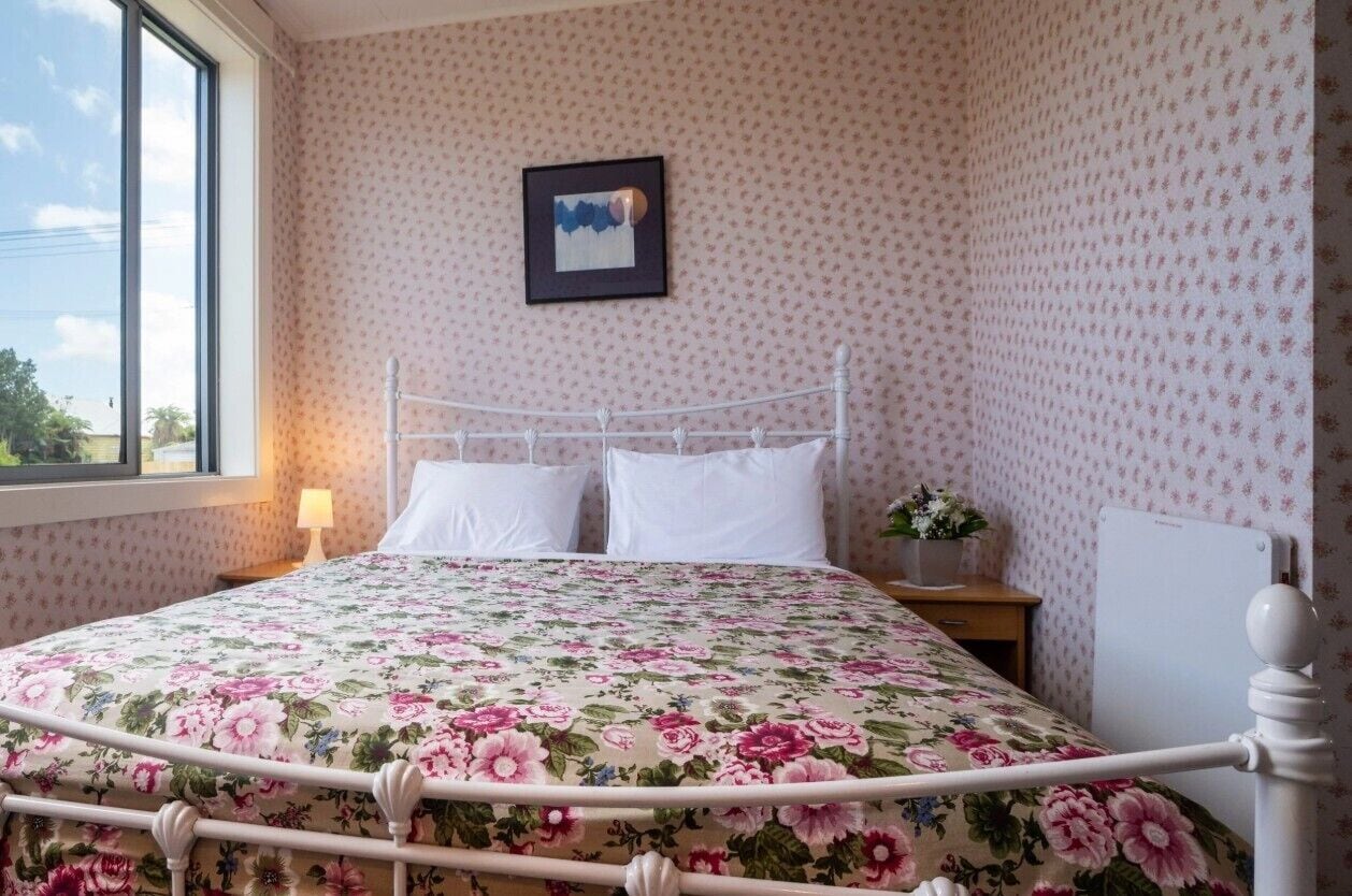 A room with a bed, a nightstand, a lamp, and a framed picture on the wall.