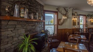 A cozy restaurant with stone walls, a fireplace, and a mounted deer head. Tables are set with cutlery and napkins.