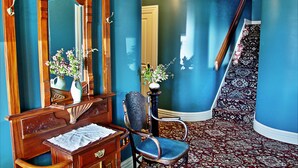 A room with a wooden desk, a chair, a mirror, and a vase with flowers.