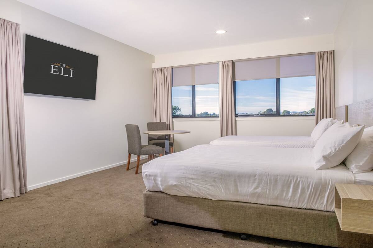 A hotel room with two beds, a TV mounted on the wall, a small table, and a chair.