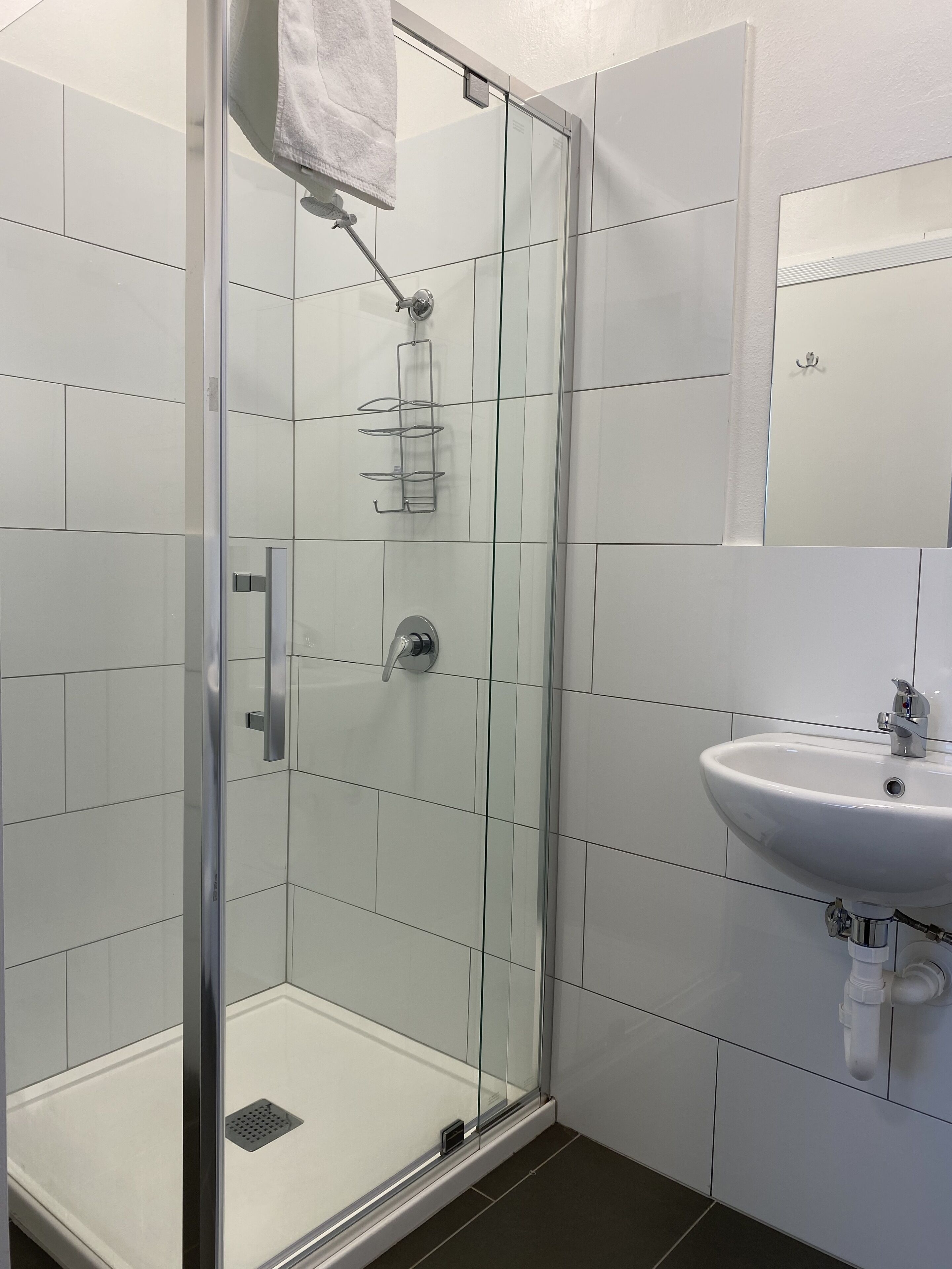 Un baño moderno con cabina de ducha de vidrio, lavabo blanco y suelo de baldosas.