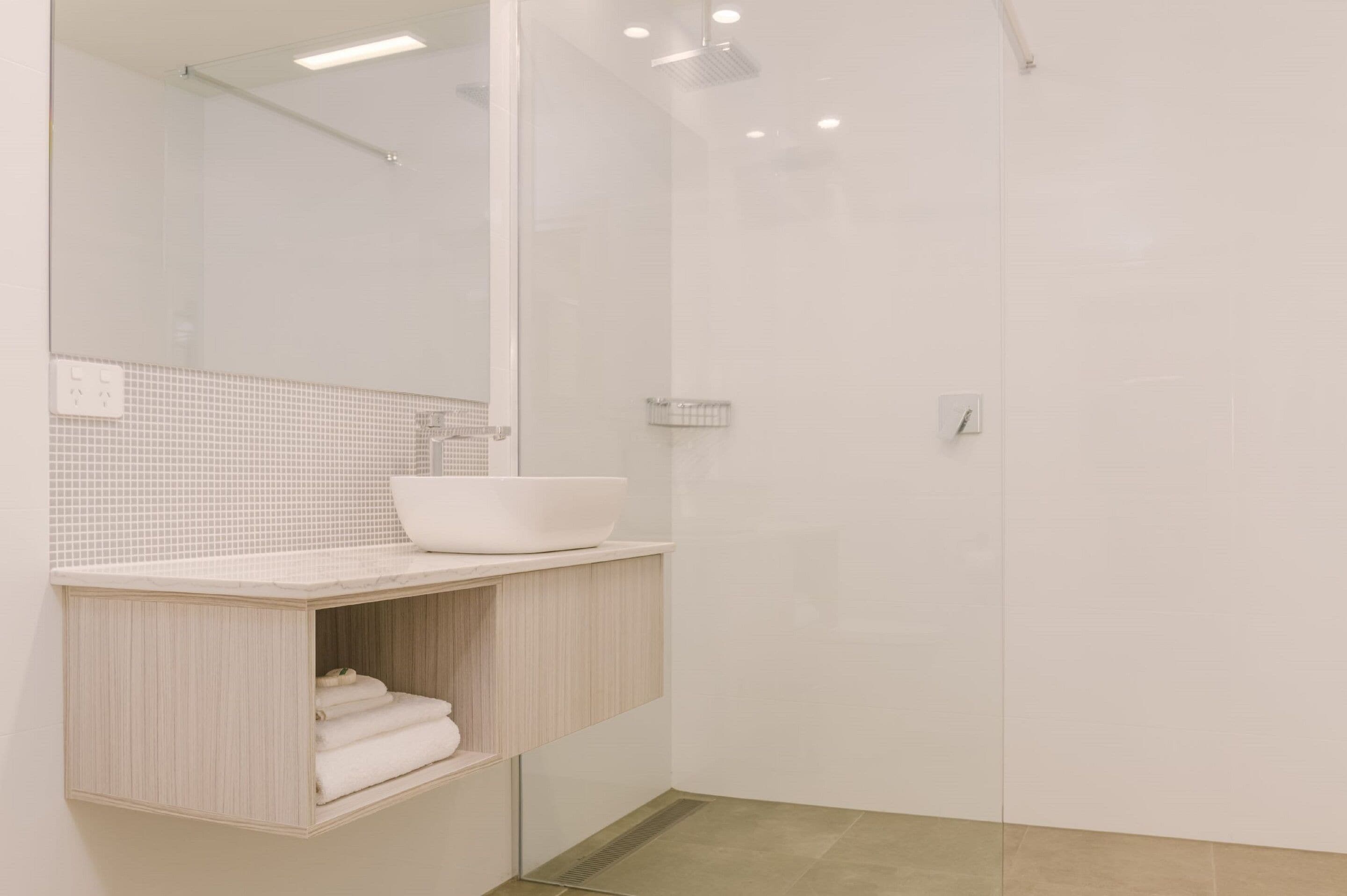 A modern bathroom with a white sink, a mirror, and a shower enclosure.