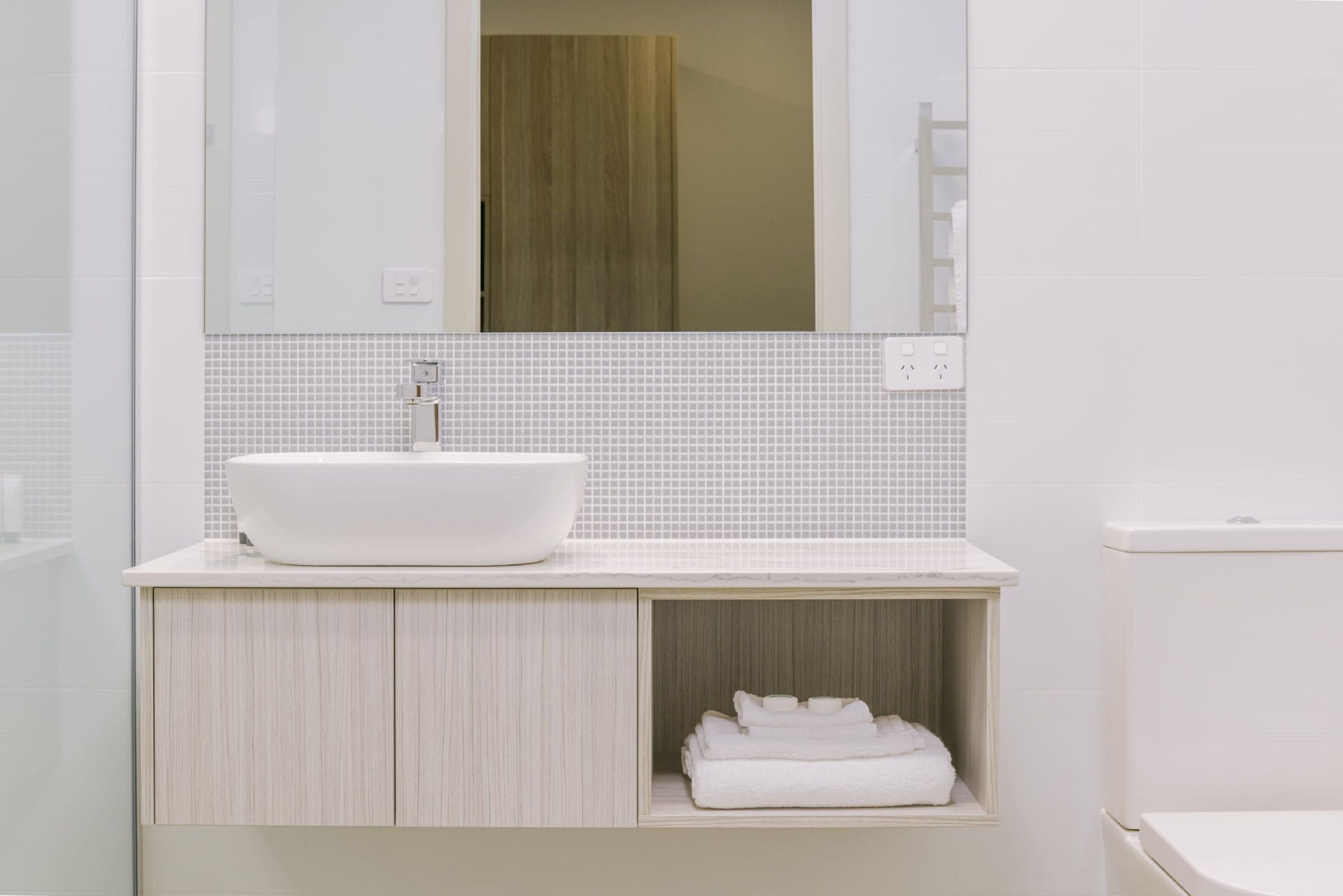 A modern bathroom with a white sink, a mirror above it, and a toilet to the right.