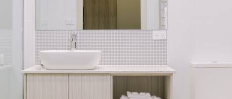 A modern bathroom with a white sink, a mirror above it, and a toilet to the right.