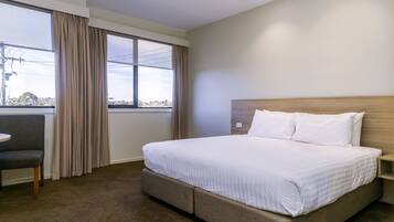 A hotel room with a large bed, a small desk, a chair, and a window with curtains.