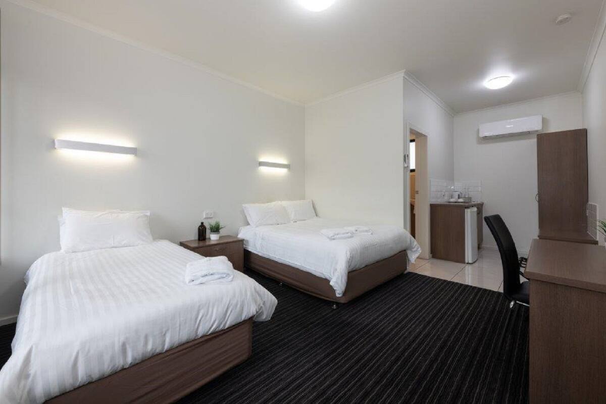 A hotel room with two beds, a desk, a chair, and a small kitchenette.