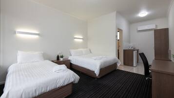 Een hotelkamer met twee bedden, een bureau, een stoel en een kleine kitchenette.