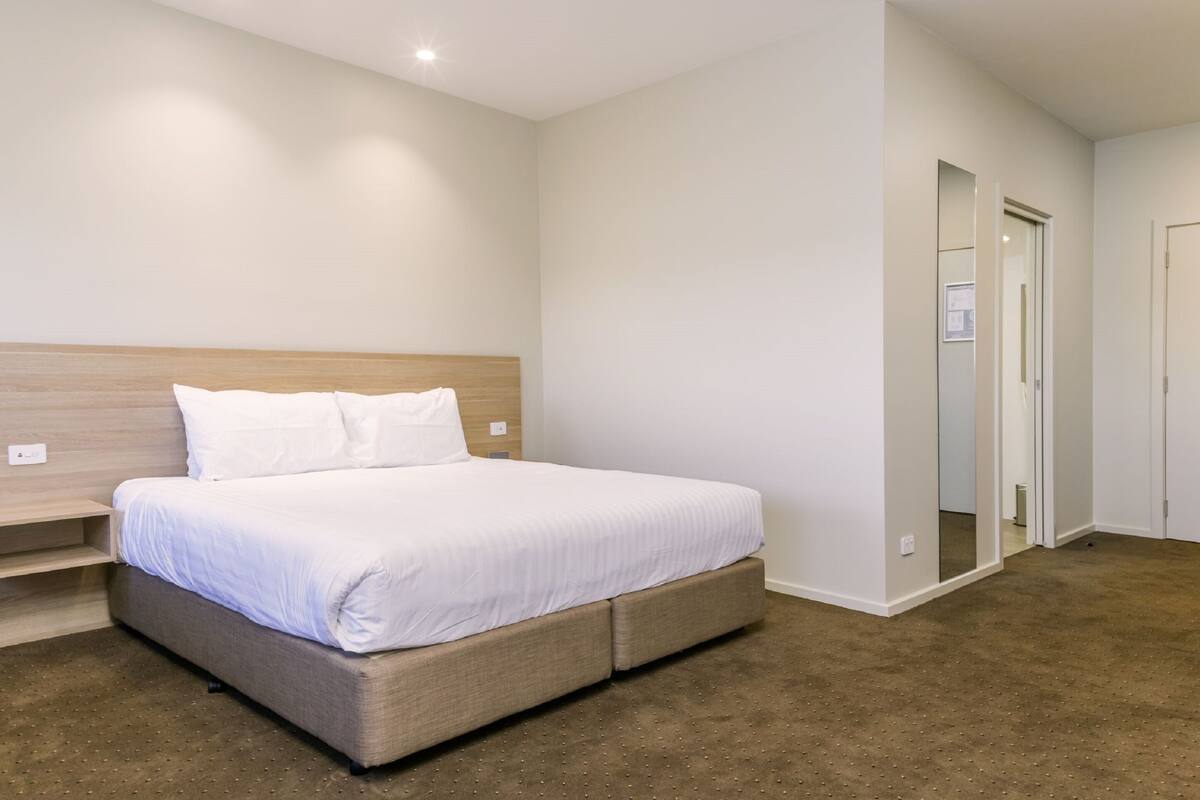 A bedroom with a bed, a wooden headboard, a carpeted floor, and a door with a mirror.