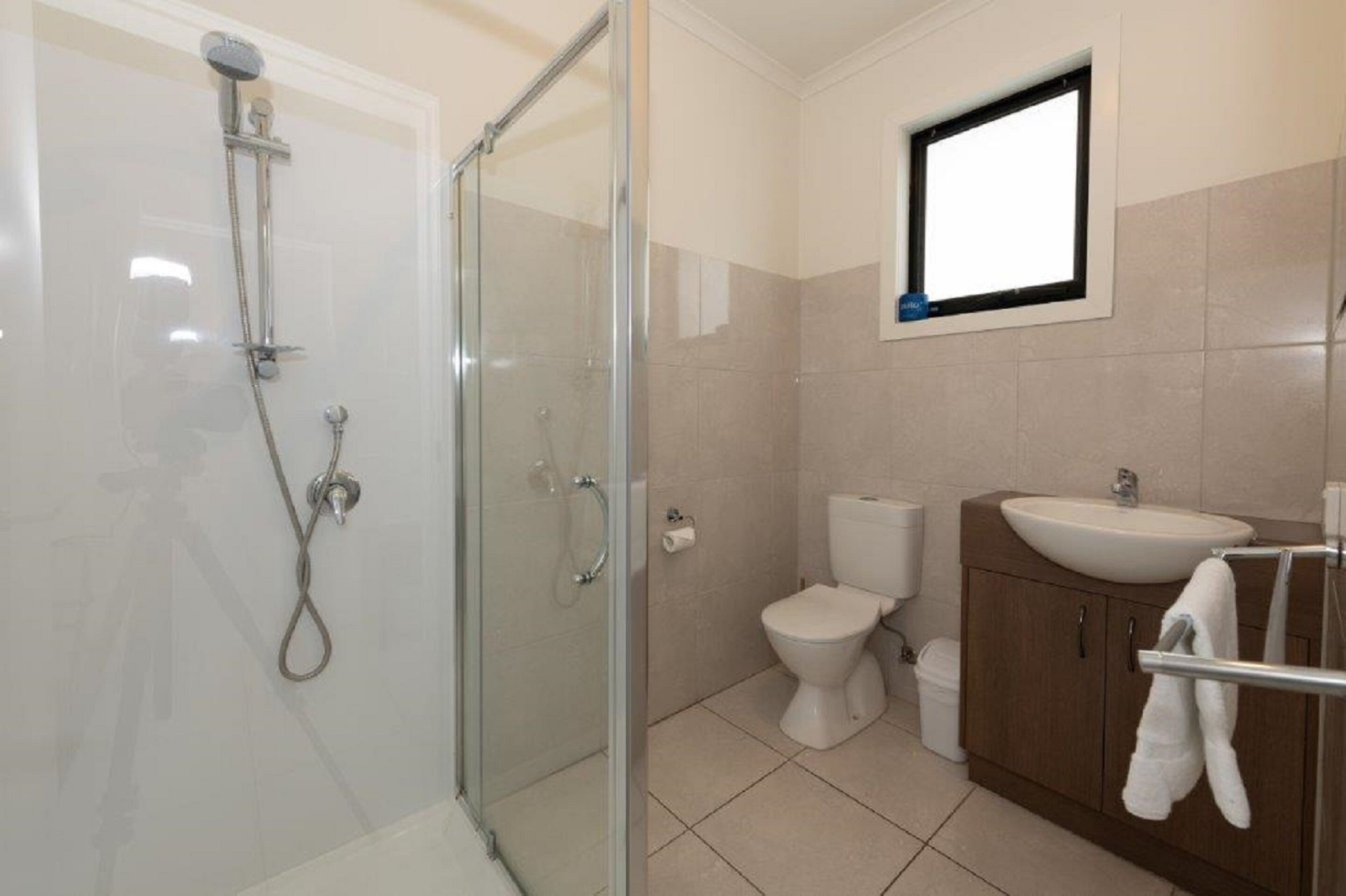 A bathroom with a glass-enclosed shower, a toilet, and a sink with a towel rack.