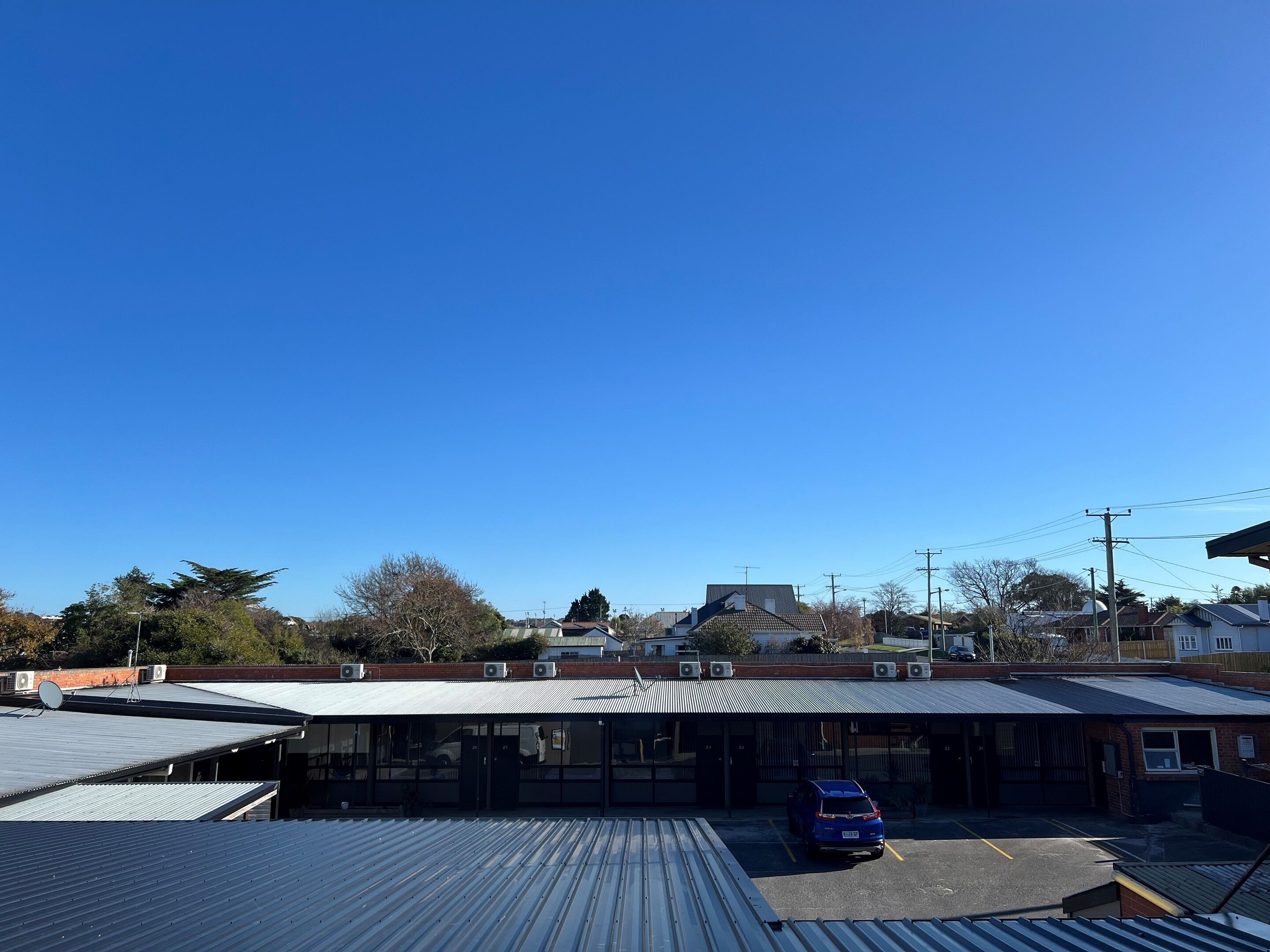 A building with a flat roof, large windows, and a parking lot with a blue car.