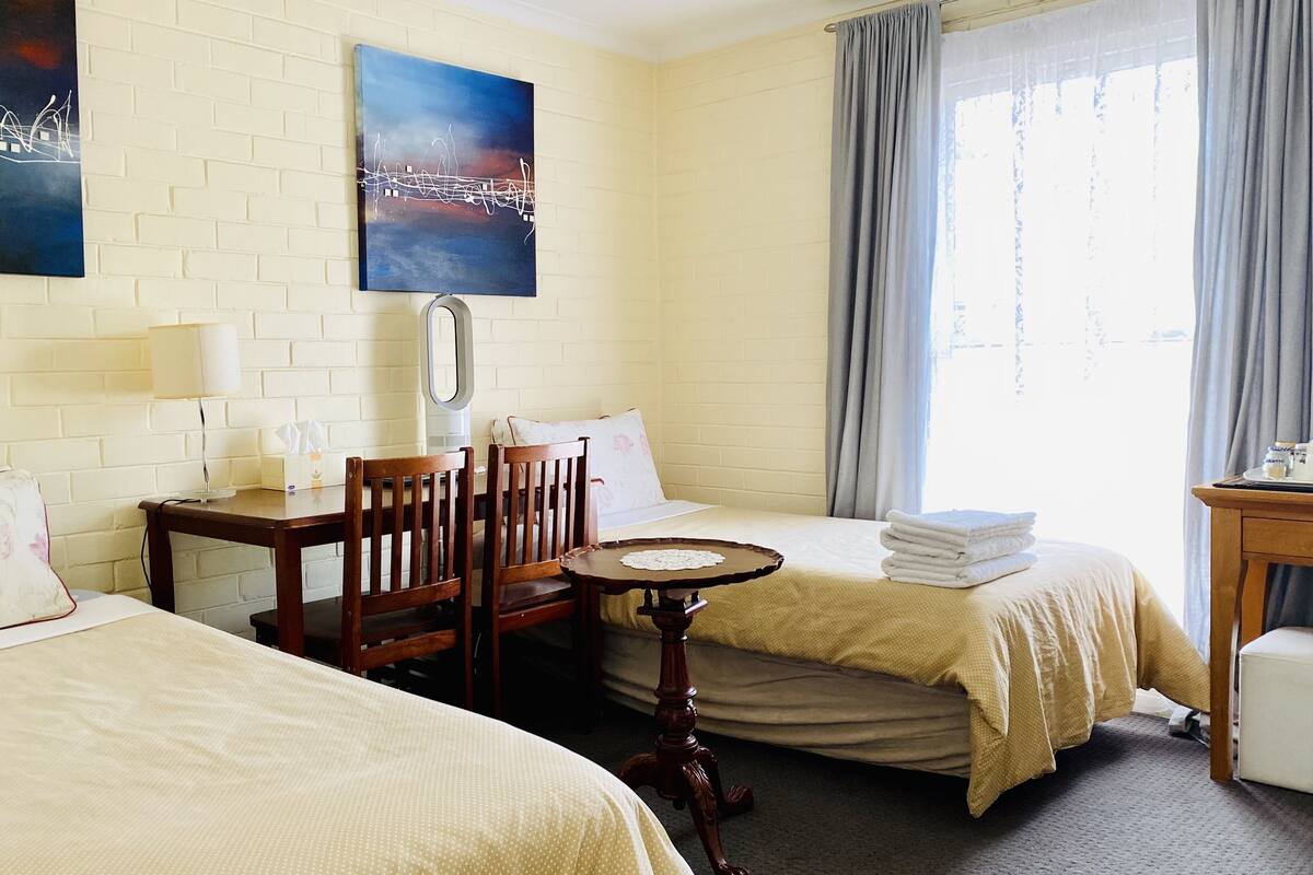 A hotel room with two beds, a desk, a chair, a small table, and a window with curtains.