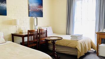 A hotel room with two beds, a desk, a chair, a small table, and a window with curtains.