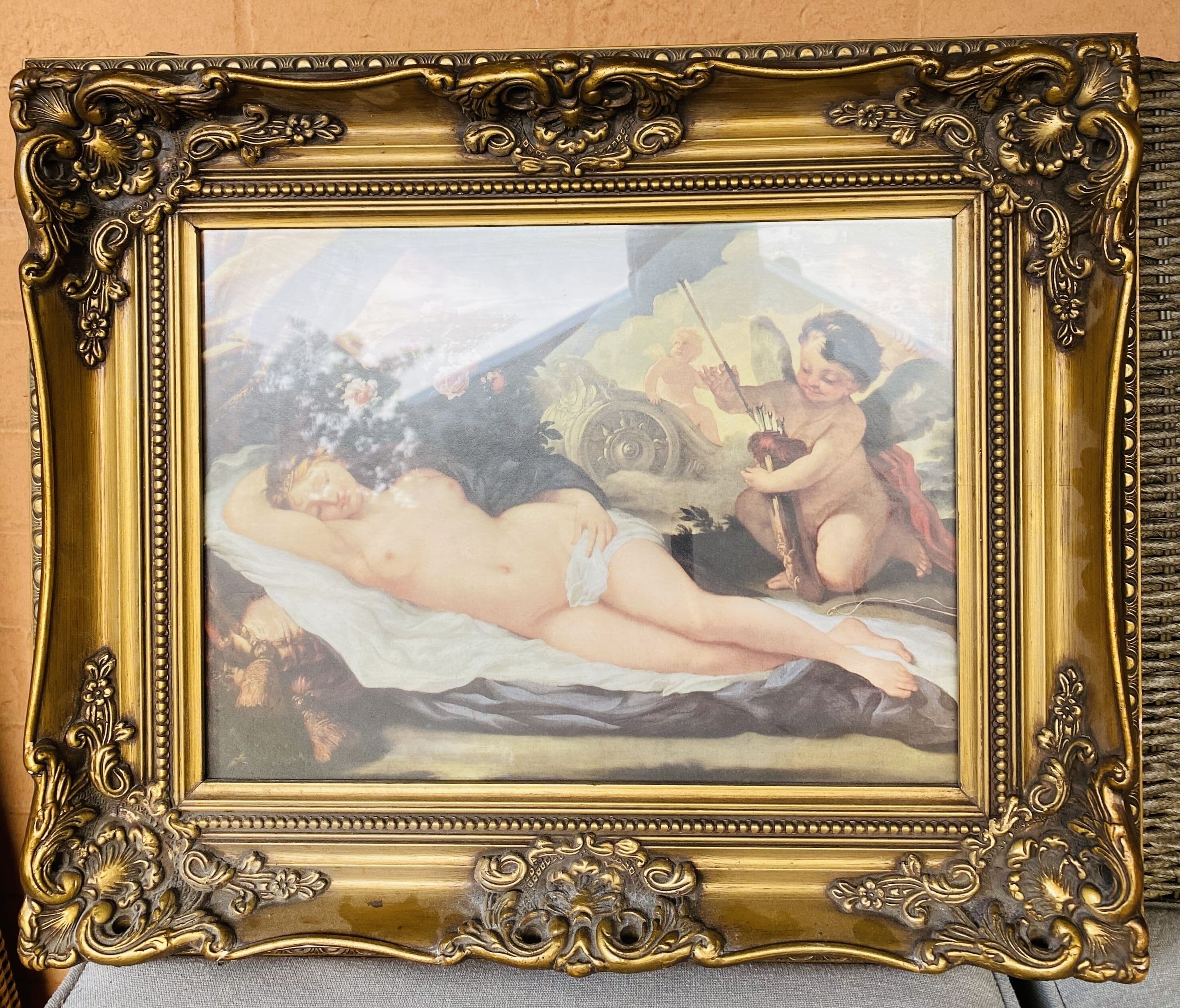 A framed painting with a classical style, featuring a reclining nude figure and cherubs.