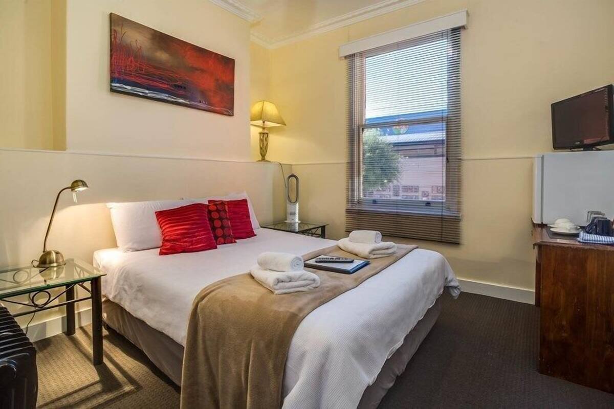 A hotel room with a bed, a desk, a lamp, a television, and a window with blinds.