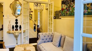 Una sala de estar acogedora con un sofá capitonado, un espejo decorativo y un cuadro de flores.