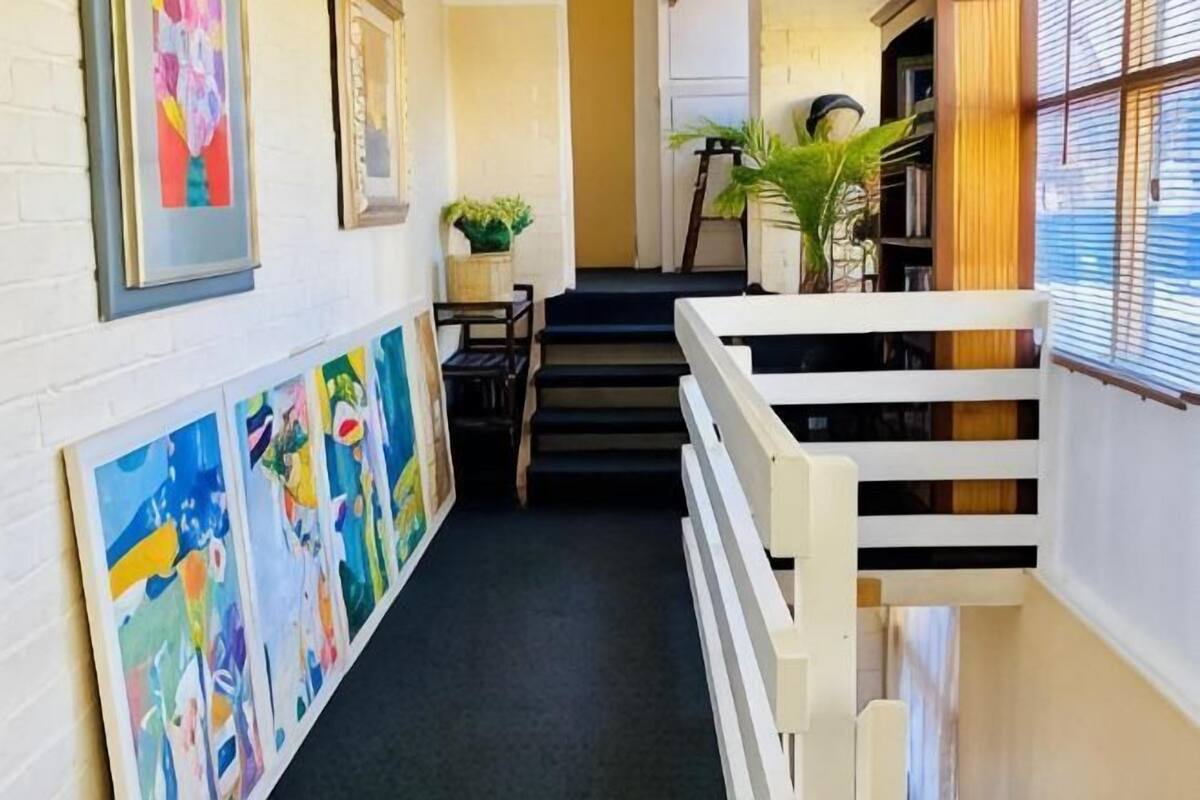 A narrow hallway with a staircase, artwork on the walls, and potted plants.