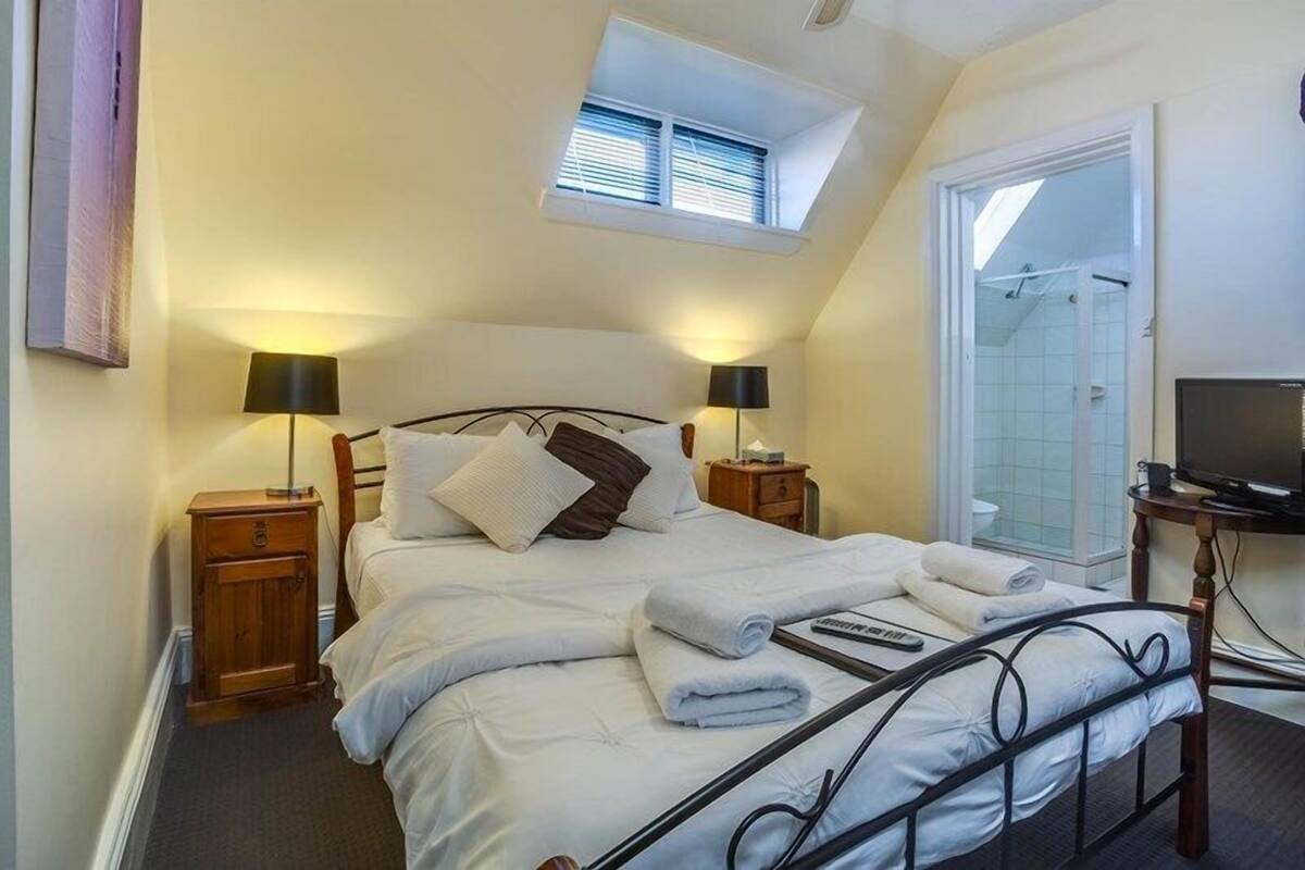 A bedroom with a bed, two bedside tables with lamps, a window, a shower area, and a television.